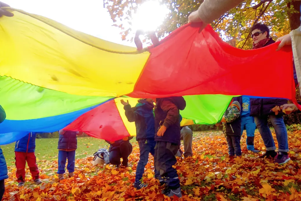 Kinder und Eltern unter einem bunten Schwungtuch im Herbstlaub